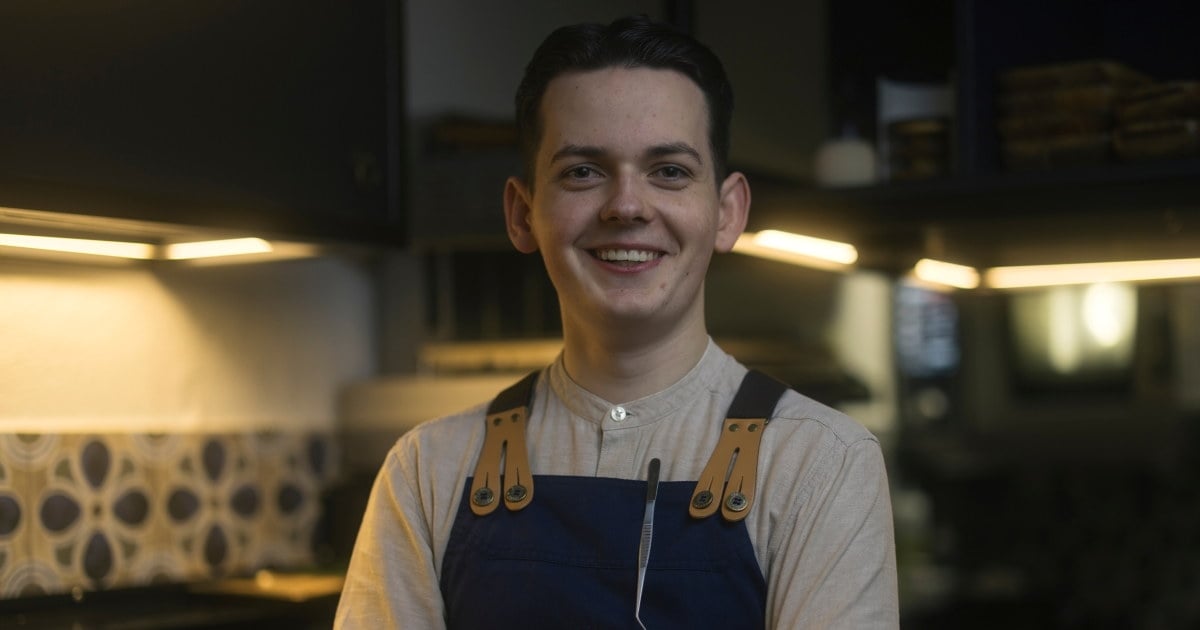 Person i forkle på et kjøkken holder hendene i kryss og smiler til kamera.